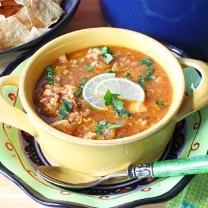 A yellow mug filled with Salsa Soup topped with limes.