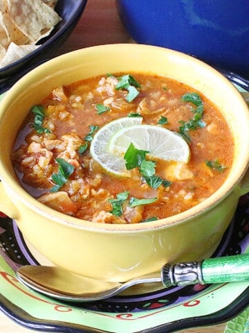 A yellow mug filled with Salsa Soup topped with limes.