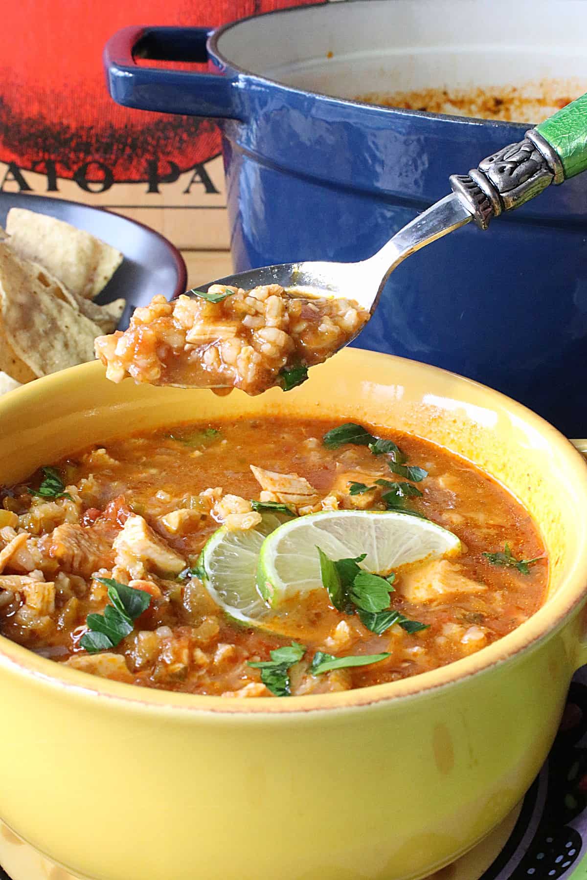 A yellow bowl of Salsa Soup in the foreground with a spoon.