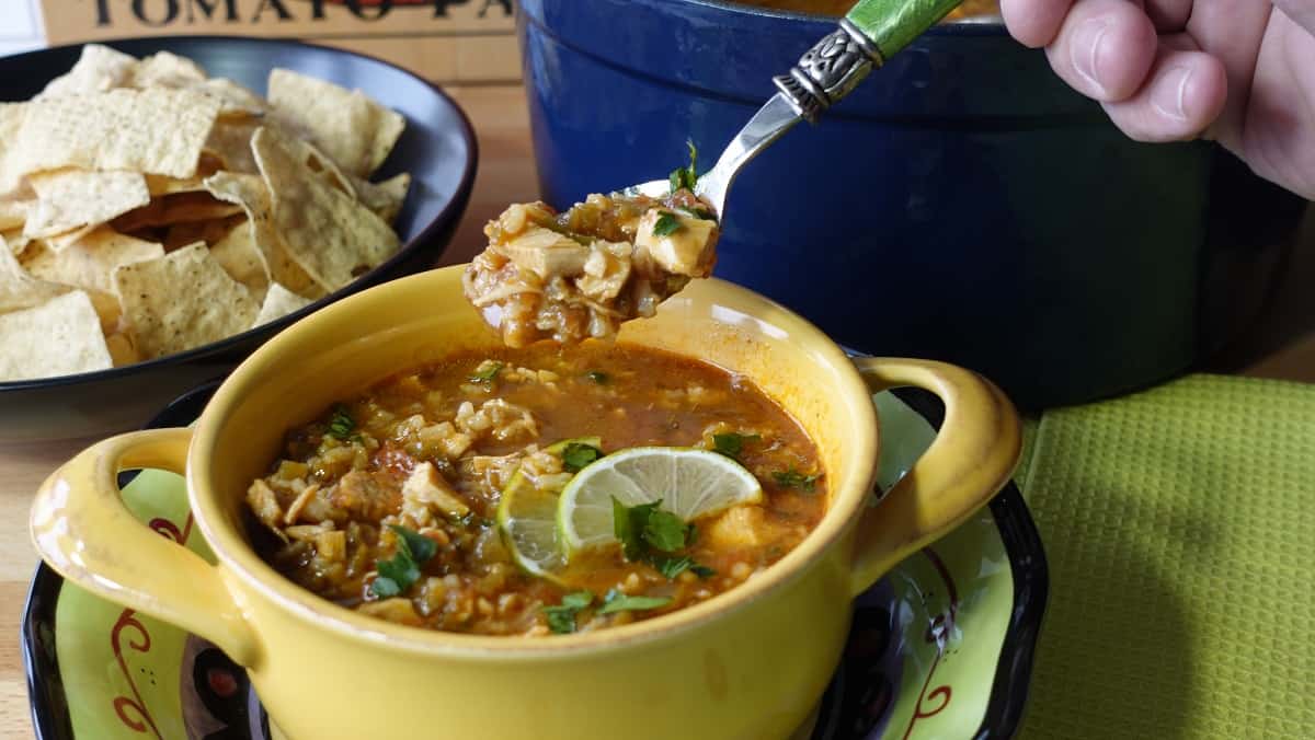 A yellow bowl filled with Salsa Soup with Chicken and Rice along with lime slices and cilantro.