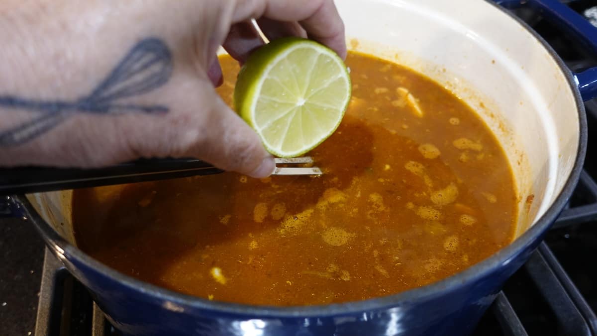 A half lime being squeezed into a pot of soup.