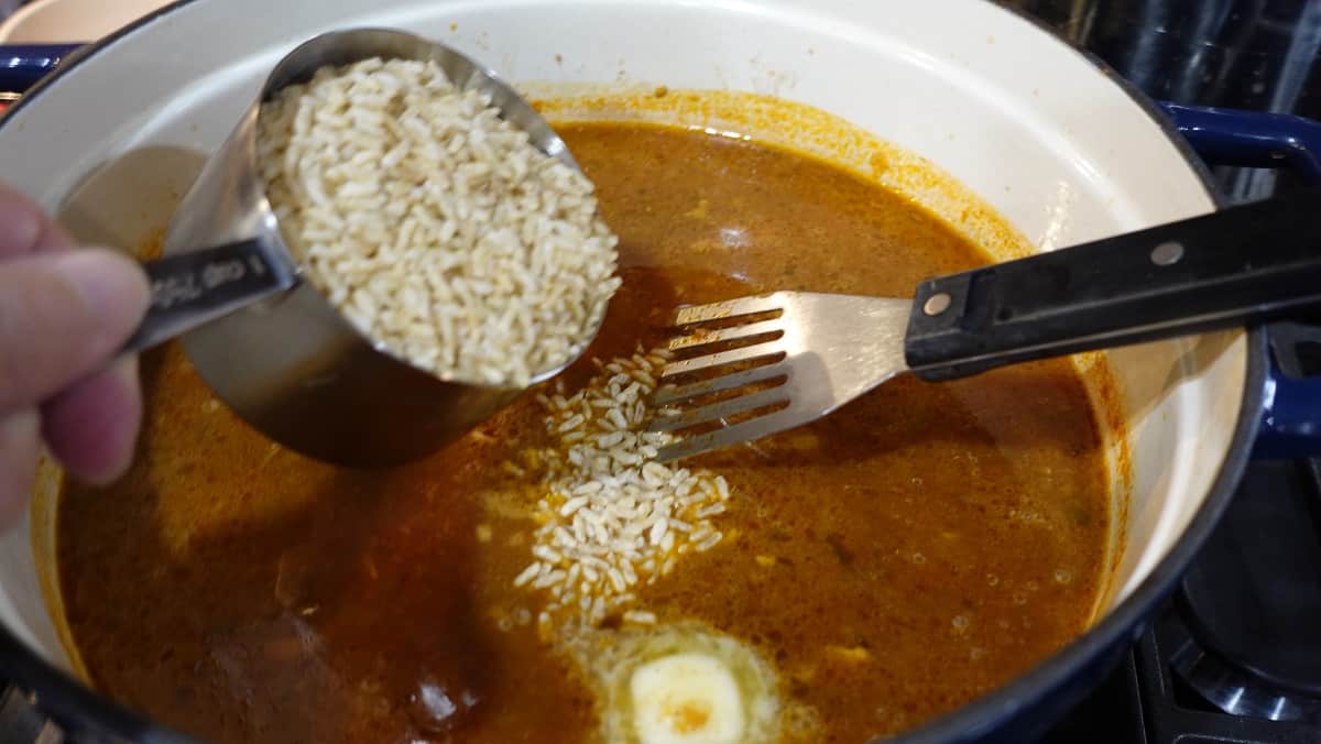 Instant rice being added to a pot of soup.