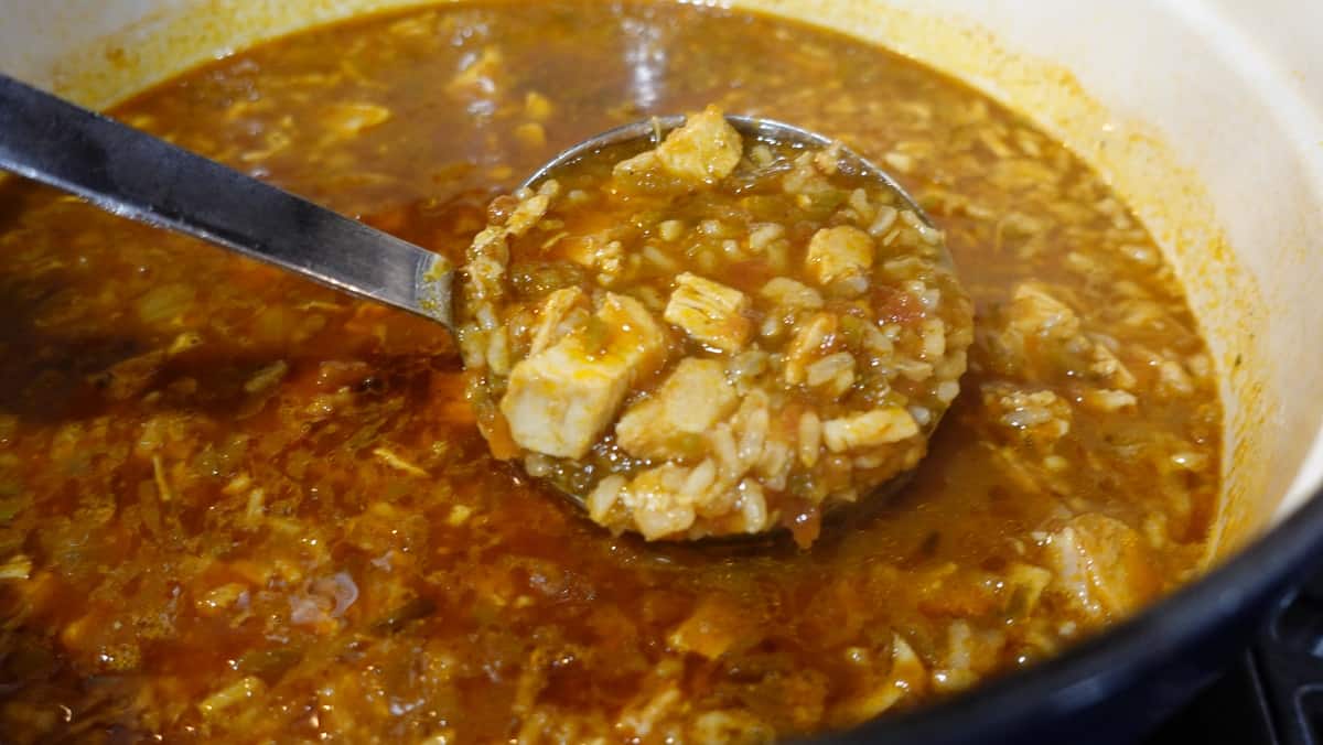 A ladle of salsa soup with chicken and rice.