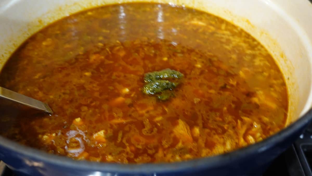 A dollop of cilantro paste in a pot of salsa soup.
