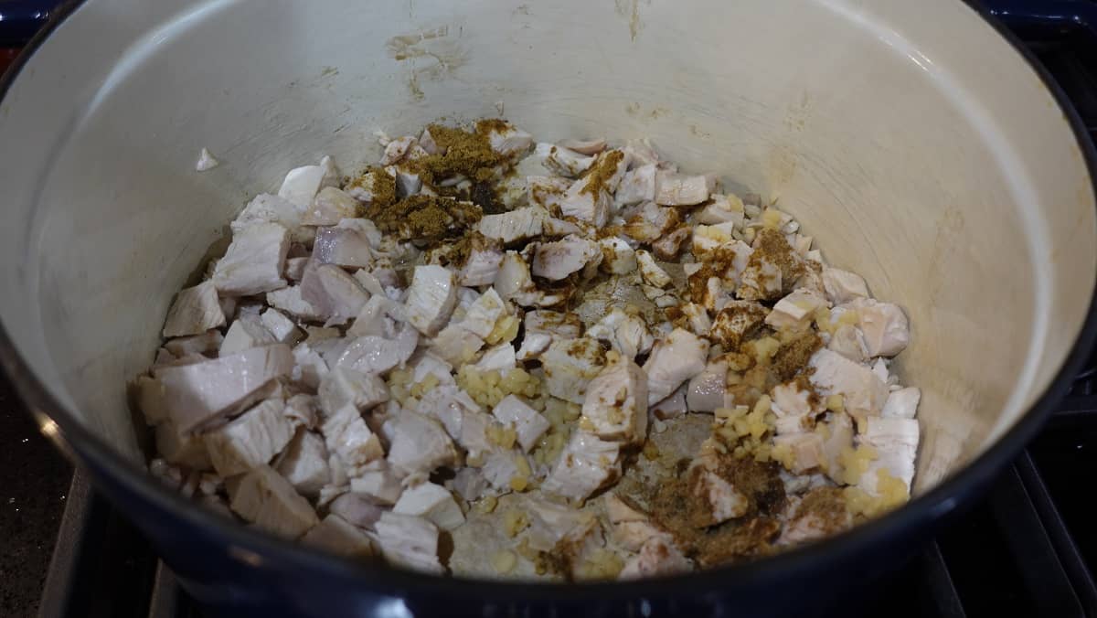 Chicken, garlic, and spices added to a Dutch oven for making salsa soup.
