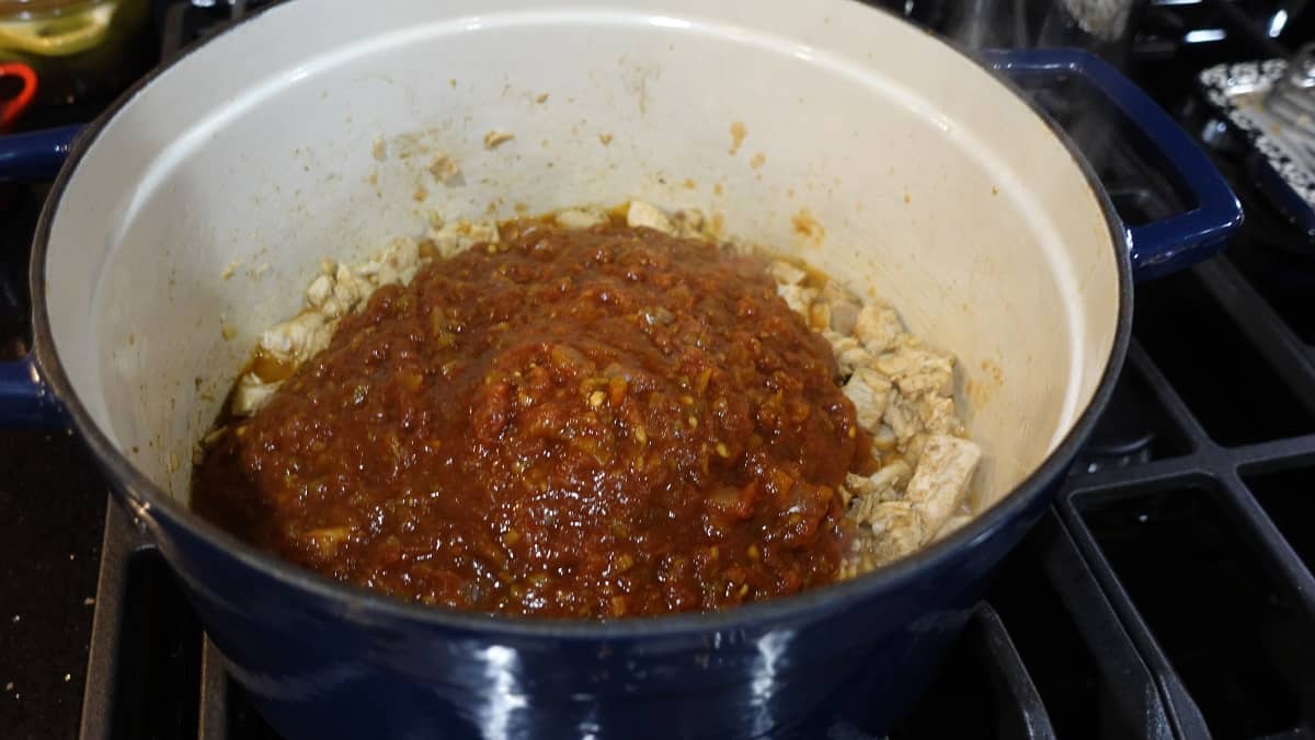 Salsa added to cooked chicken in a stockpot on the stovetop.