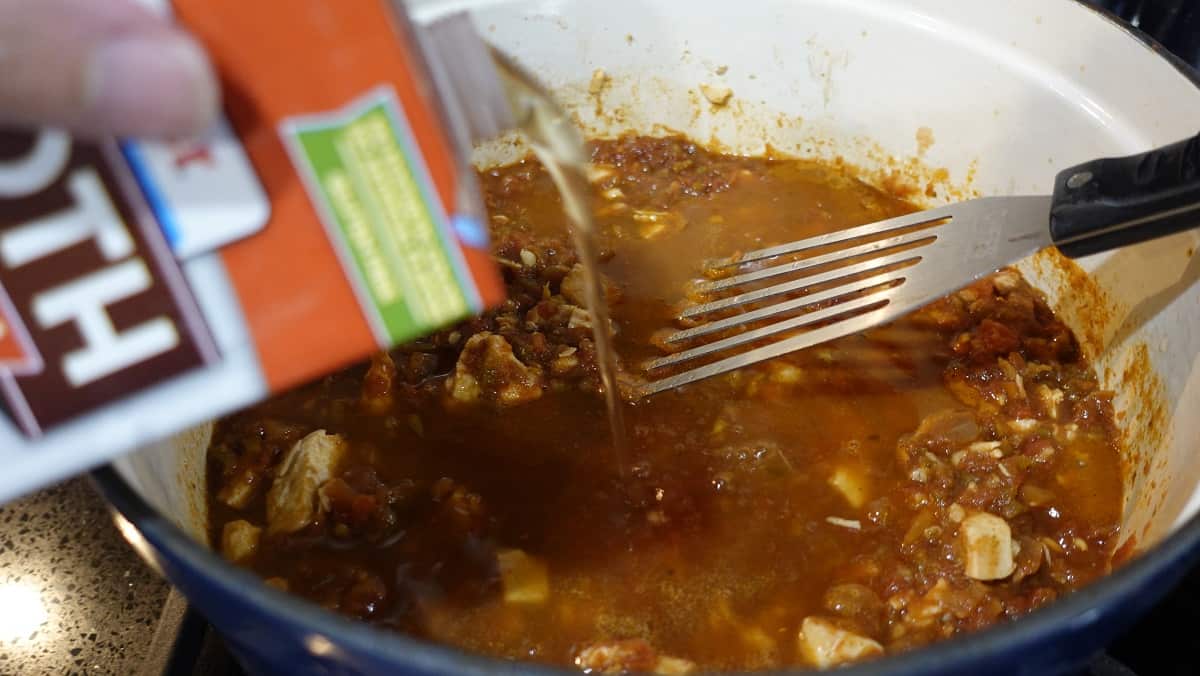 Chicken broth being added to a pot of salsa soup.