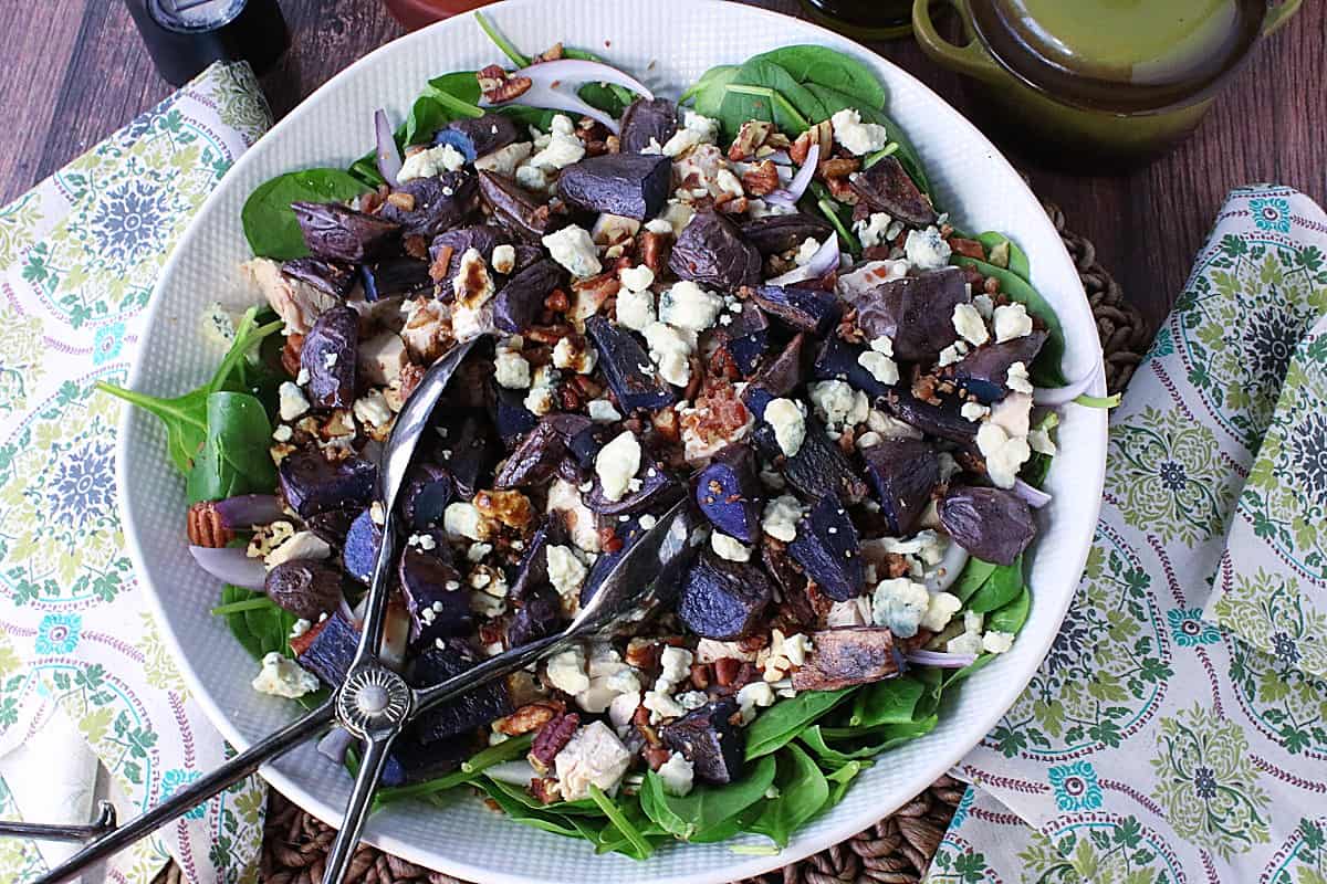 A round white bowl filled with Spinach Salad with Blue Cheese and Purple Potatoes.