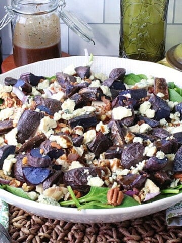 A beautiful bowl of spinach salad with purple potatoes, pecans, blue cheese, and sliced onions.