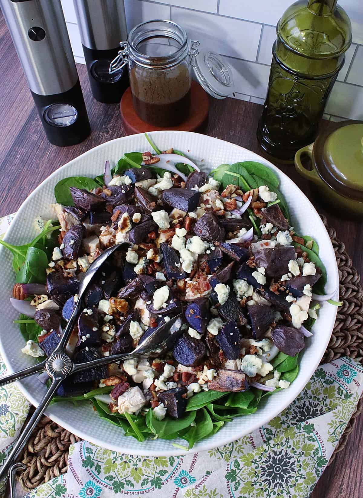 A spinach salad with tongs in a bowl.