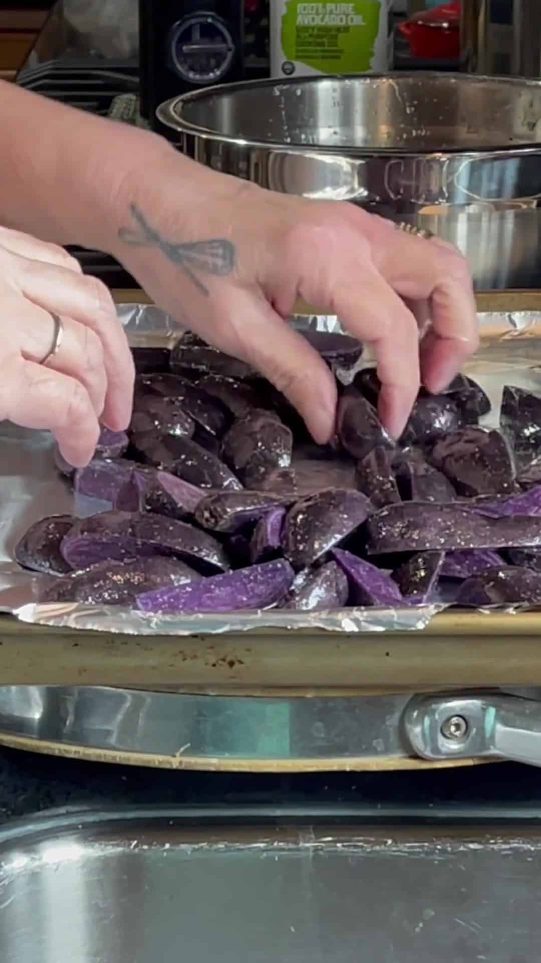 Purple potatoes being arranged on a baking sheet.