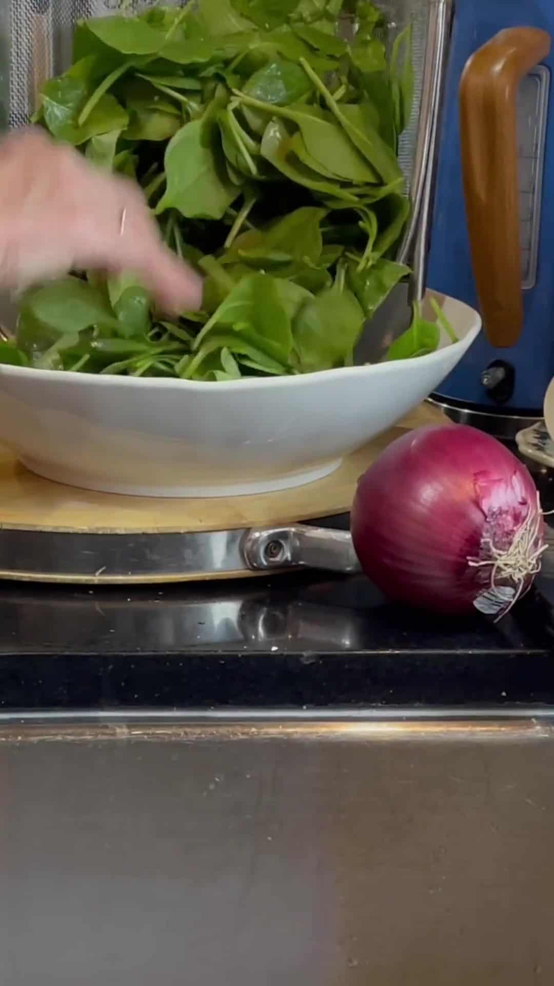 Fresh spinach being placed in a large white bowl.