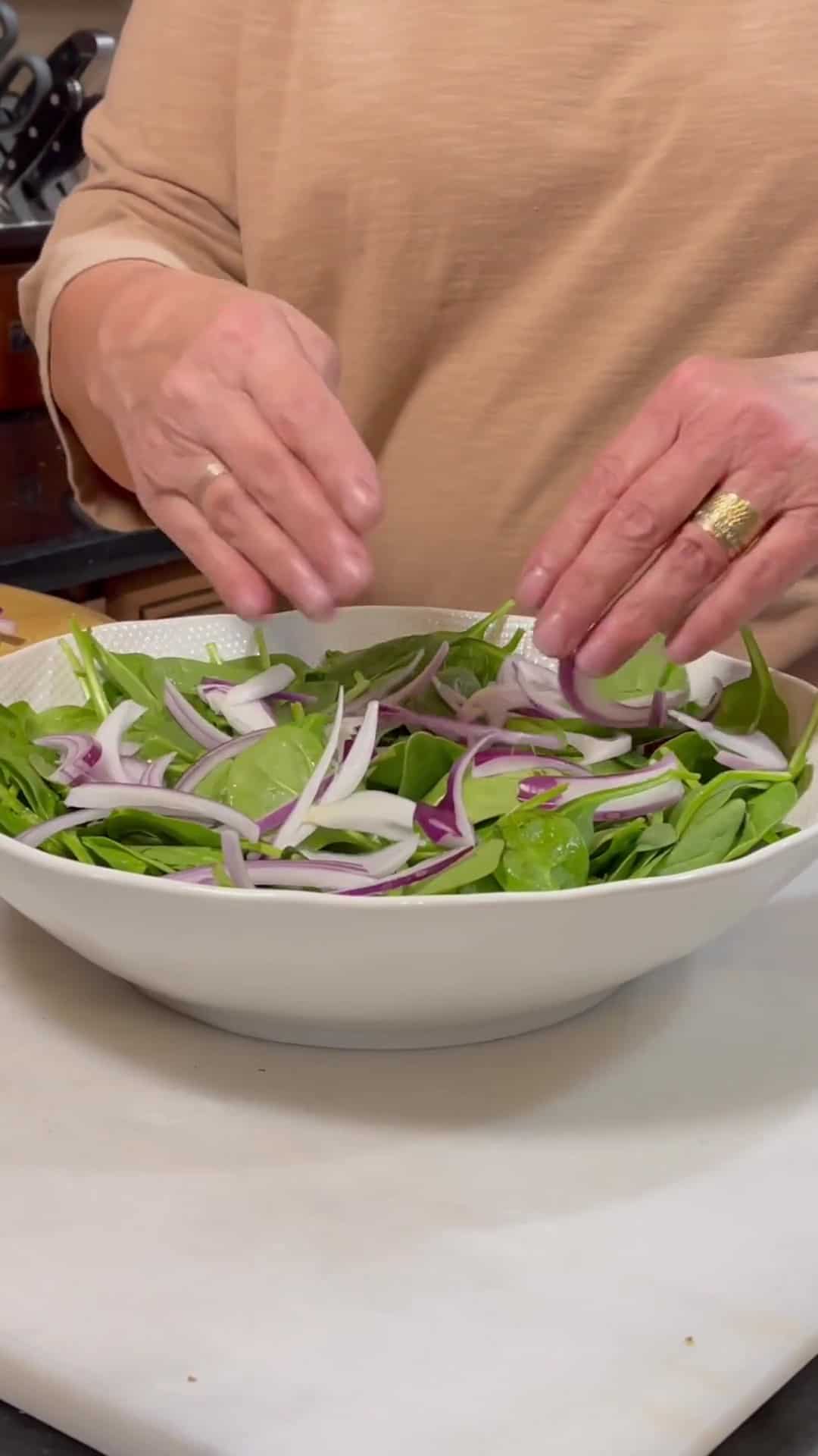 Red onion slices being placed onto a spinach salad.