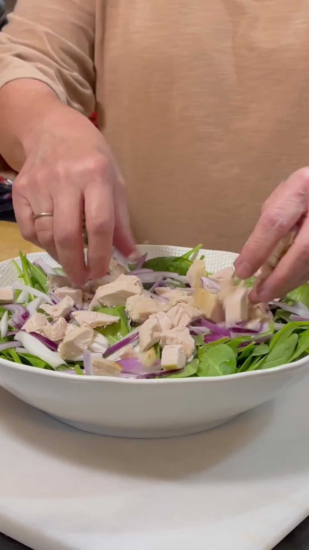 Chopped cooked chicken being added to a salad bowl.