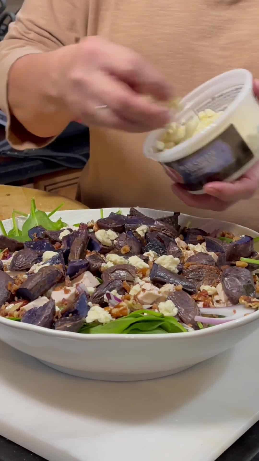 Blue cheese crumbles being added to a spinach salad.