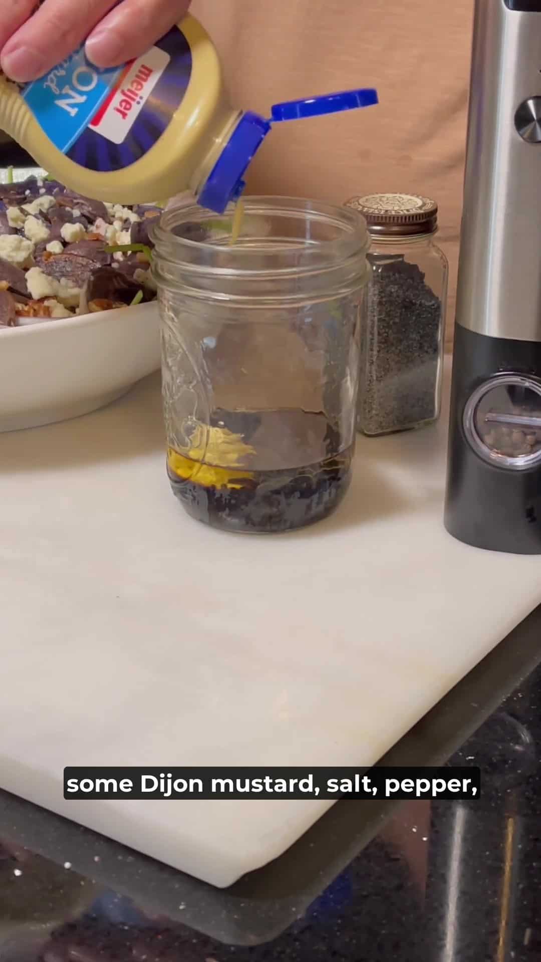 Dijon mustard being squirted into a mason jar to make a vinaigrette.