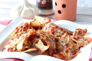 A square white plate filled with Pizza Nachos covered in pepperoni and melted cheese.