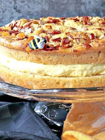 A German Bee Sting Cake with a cream center and honey almond topping on a glass pedestal.