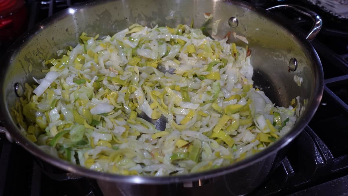 Fried cabbage and leeks in a large skillet on a stovetop.