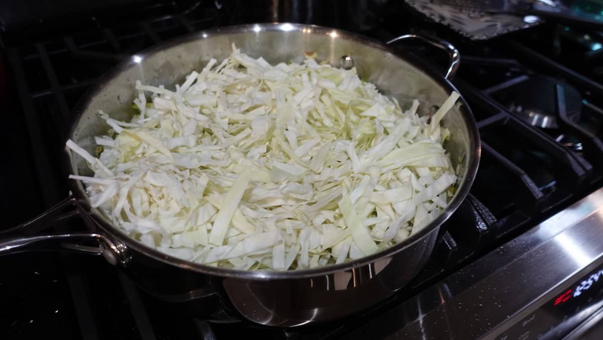 Shredded cabbage in a large skillet on a stovetop.