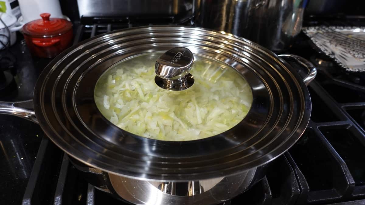 A large skillet filled with shredded cabbage with a lid on top.