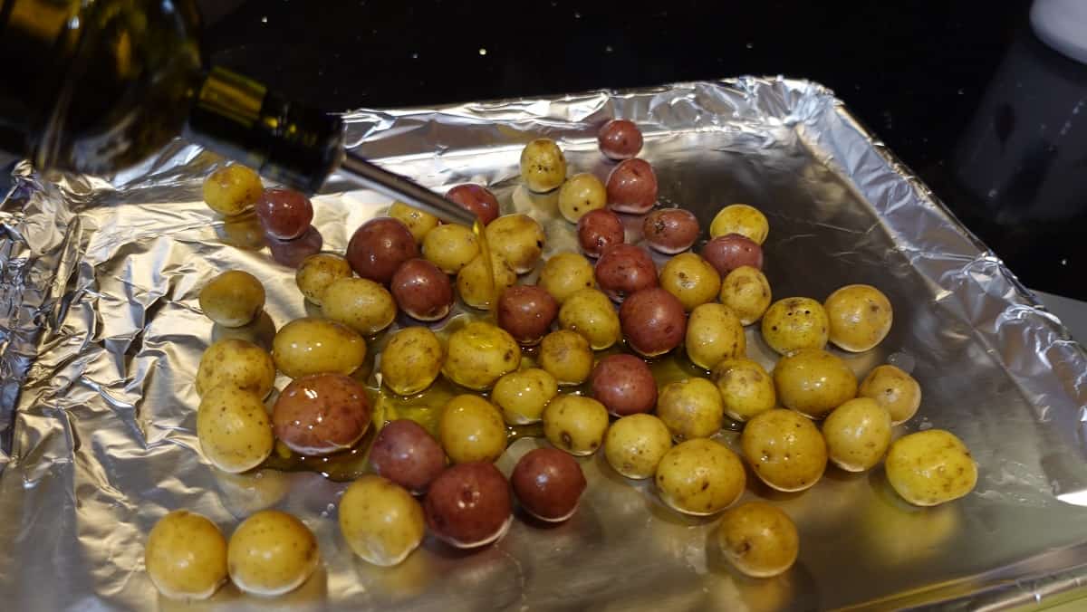 Image of baby potatoes on a baking sheet with foil being drizzled with oil for cooking.