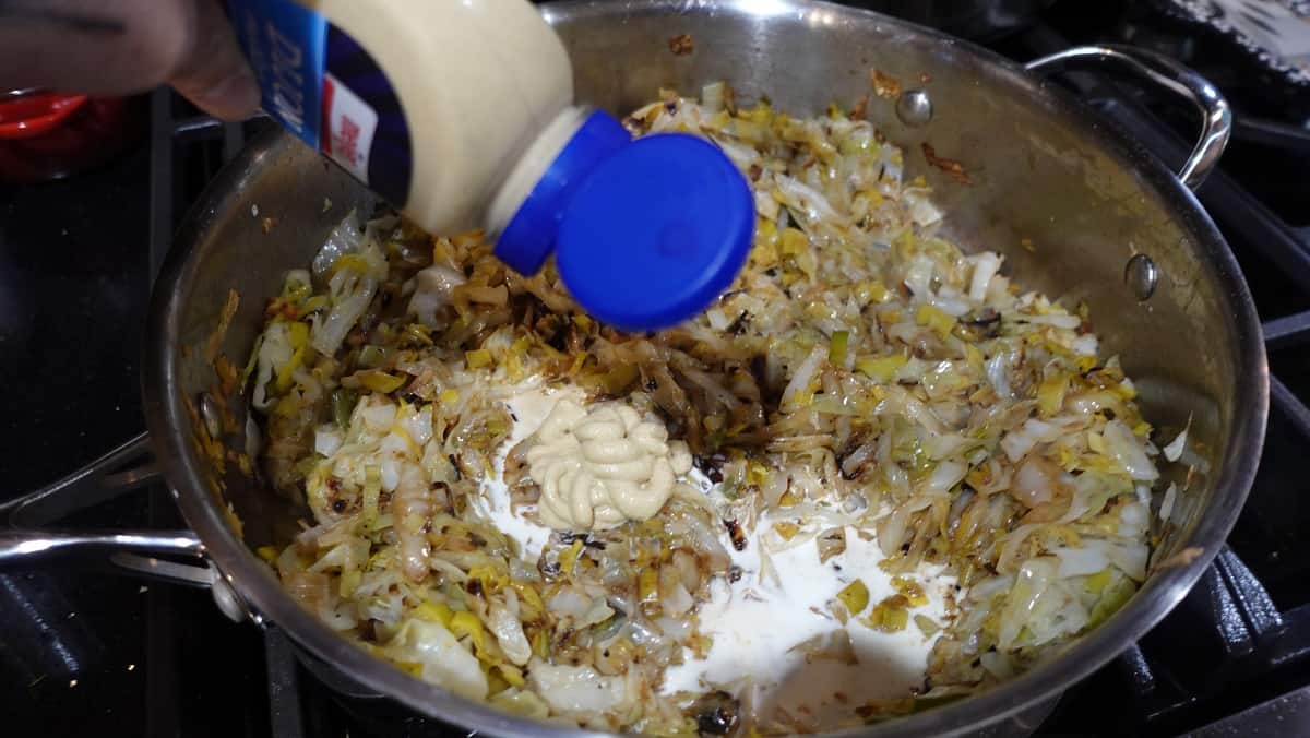 Dijon mustard being added to a skillet with fried cabbage and leeks.