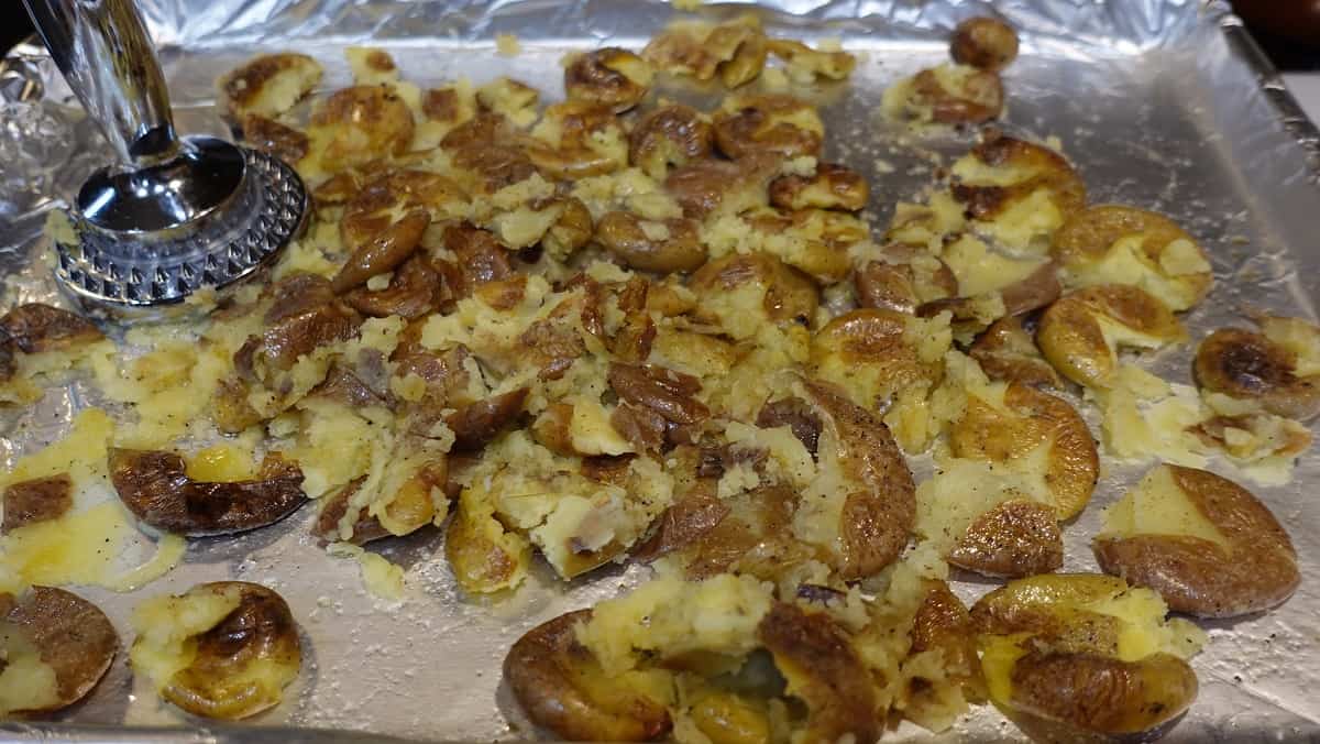 A meat mallet on a baking sheet along with roasted smashed potatoes.