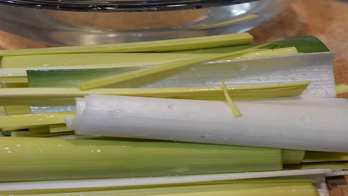 Freshly washed leeks on a cutting board ready to be sliced.