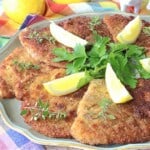 Breaded Pork Schnitzel on a platter with thyme and lemon wedges.