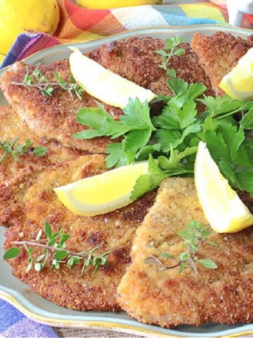 Breaded Pork Schnitzel on a platter with thyme and lemon wedges.