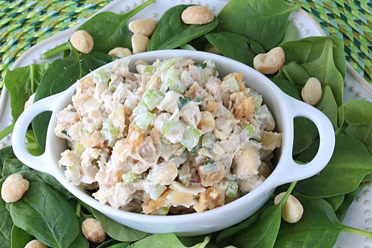 A small white casserole dish filled with Hawaiian Chicken Salad, surrounded by macadamia nuts.