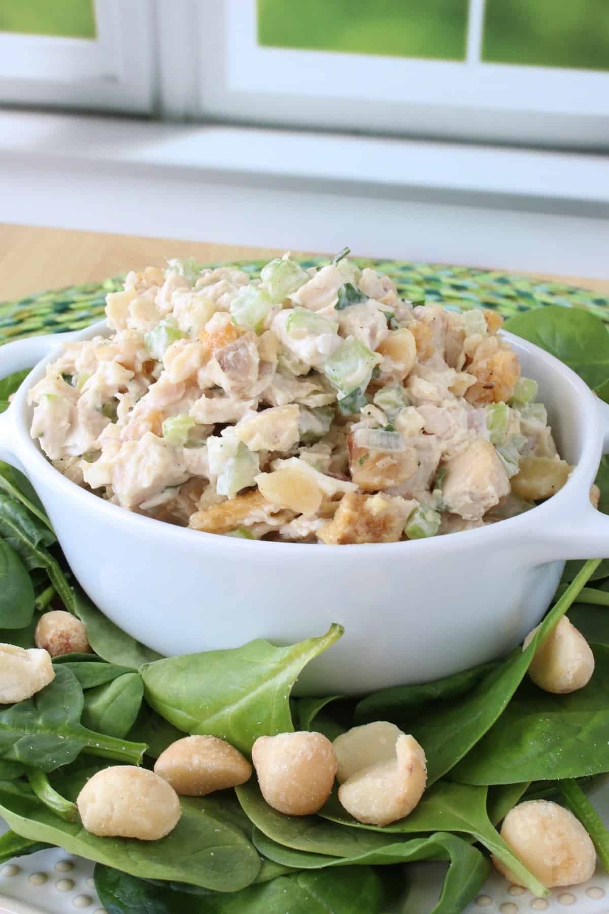 Fresh spinach leaves and macadamia nuts on a plate along with chicken salad with pineapple and macadamia nuts.