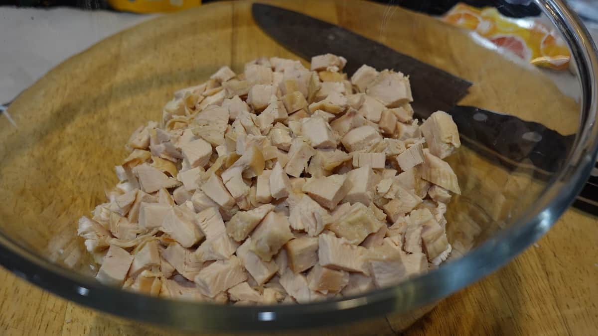 Cut up cooked chicken in a glass bowl.