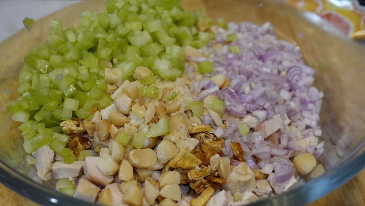 Diced celery, chicken, macadamia nuts and shallots in a glass bowl.