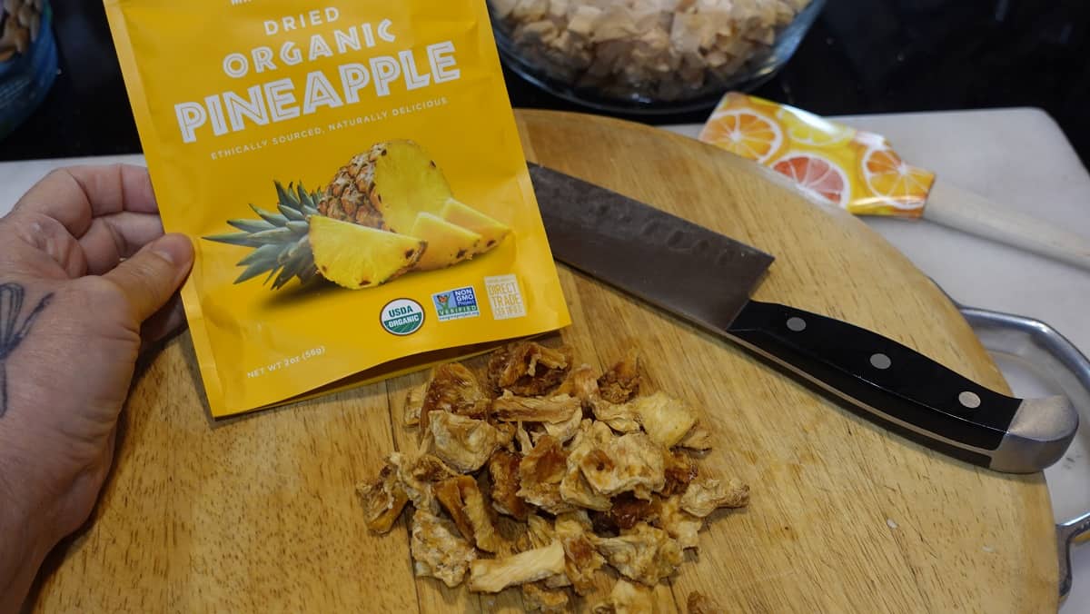 A bag of organic dried pineapple on a cutting board with a knife.