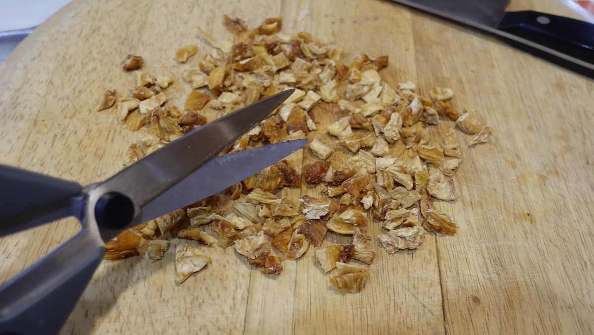 Scissors and diced dried pineapple on a cutting board.