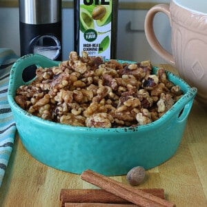A blue ceramic bowl filled with Roasted Cinnamon Walnuts with a napkin on the side.