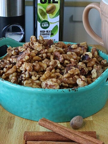 A blue ceramic bowl filled with Roasted Cinnamon Walnuts with a napkin on the side.