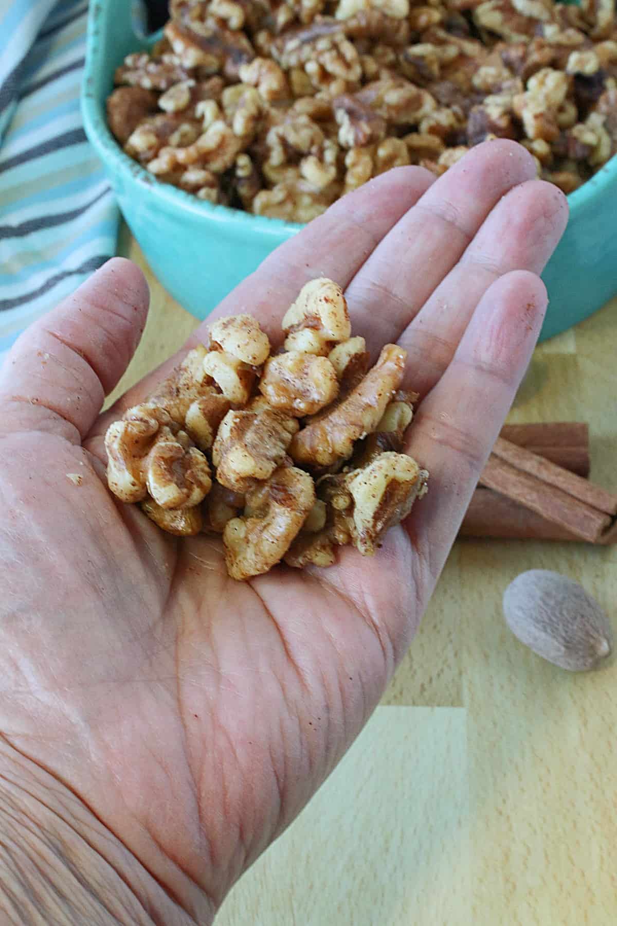 A hand holding a serving of Healthy Cinnamon Roasted Walnuts.