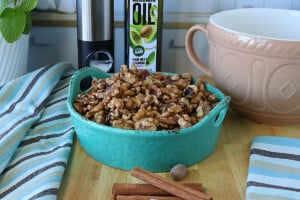 A Blue bowl of cinnamon roasted walnuts in the front of a salt mill and bottle of avocado oil.