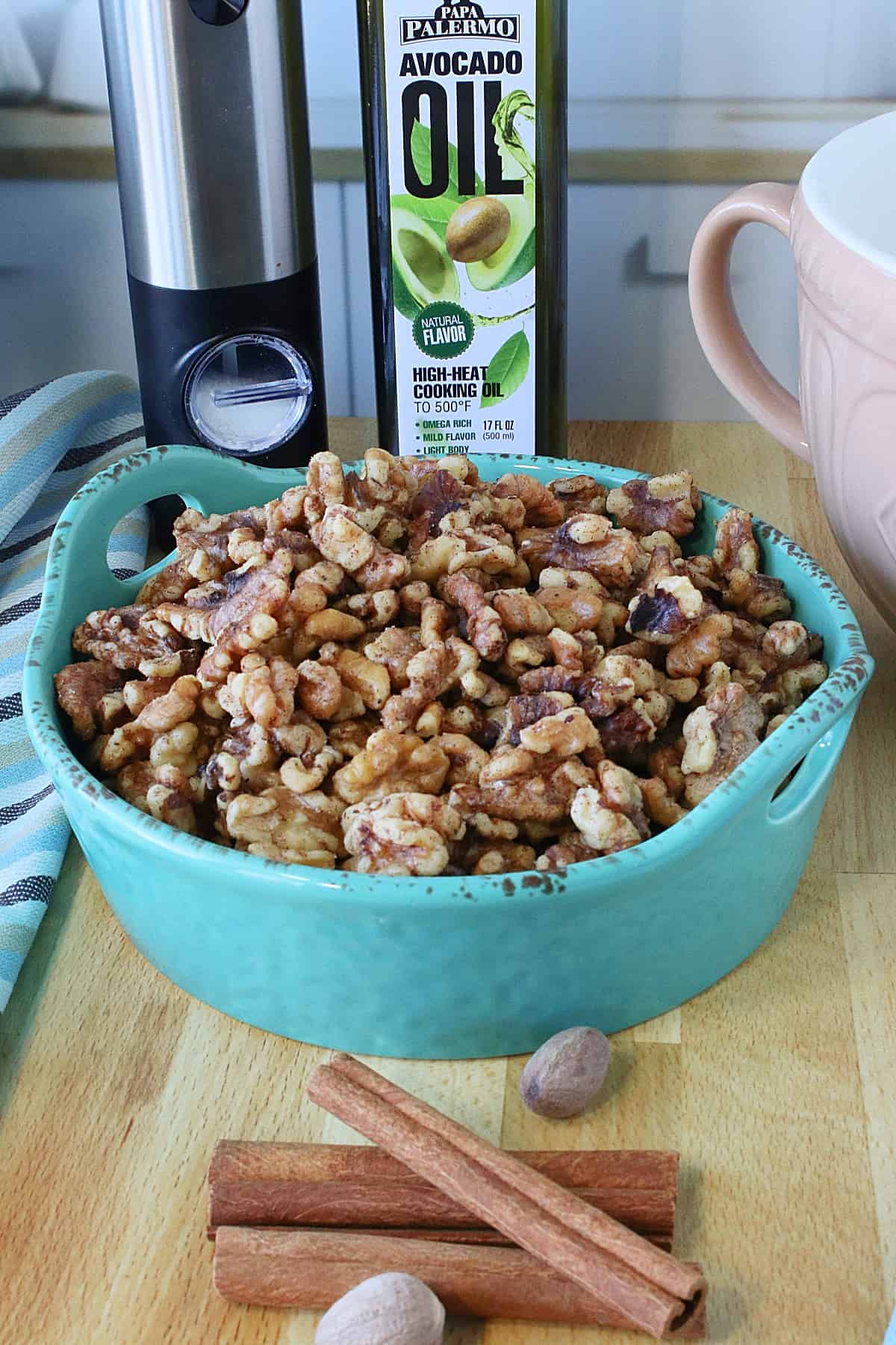 Cinnamon sticks and nutmeg pods in front of a bowl of Cinnamon Roasted Walnuts.