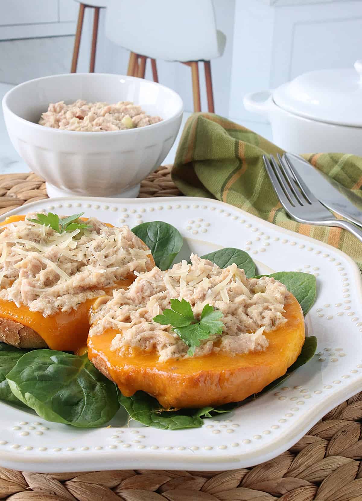 A white Swiss dot plate with an open face Bagel Tuna Melt sandwich.