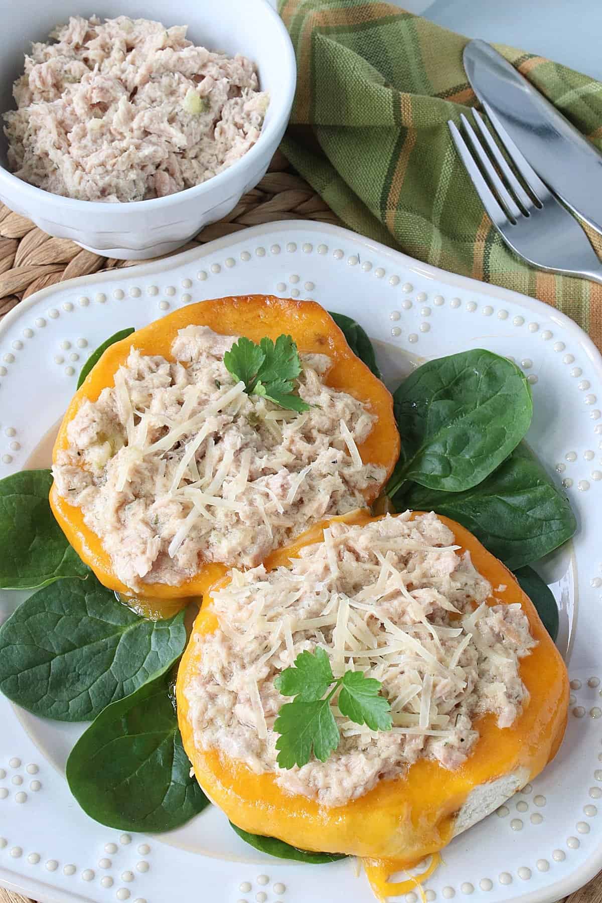 Melted cheddar cheese on a bagel and topped with tuna salad.