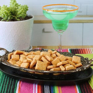 A glass and metal dish filled with square shaped Cornbread Crackers.