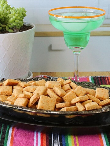 A glass and metal dish filled with square shaped Cornbread Crackers.