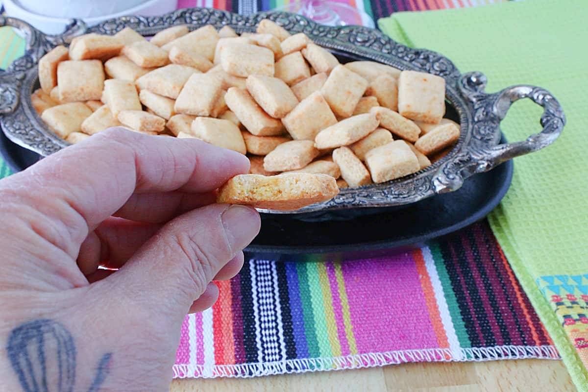A hand holding a homemade cornbread cracker with a bite taken from it.