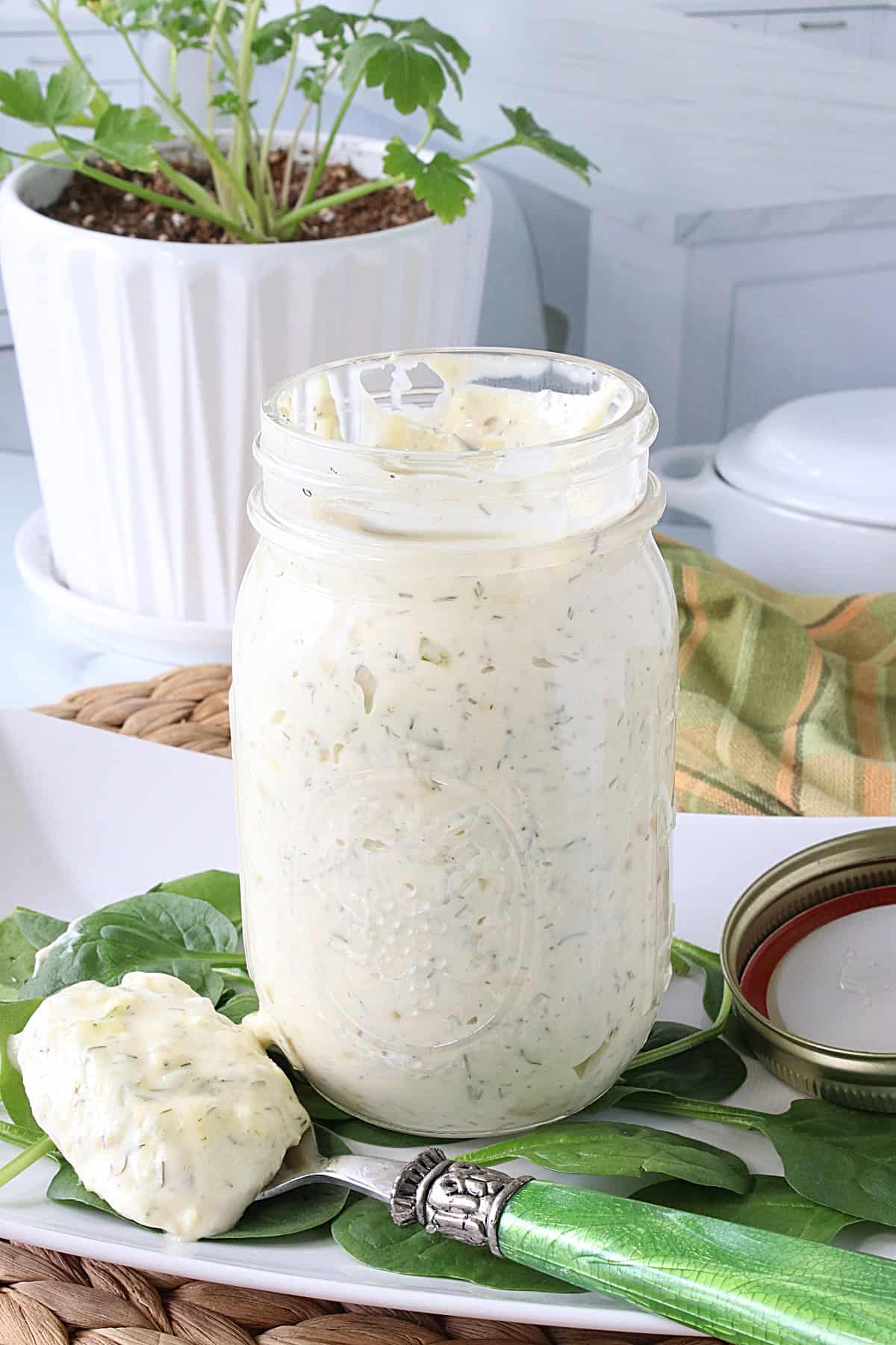 A glass jar filled with Homemade Dill Tartar Sauce along with a spoonful in front.