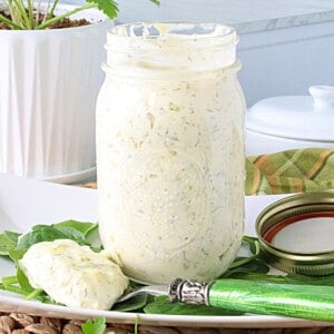A glass mason jar filled with Homemade Dill Tartar Sauce with flecks of dill in the sauce.