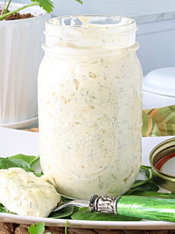 A glass mason jar filled with Homemade Dill Tartar Sauce with flecks of dill in the sauce.